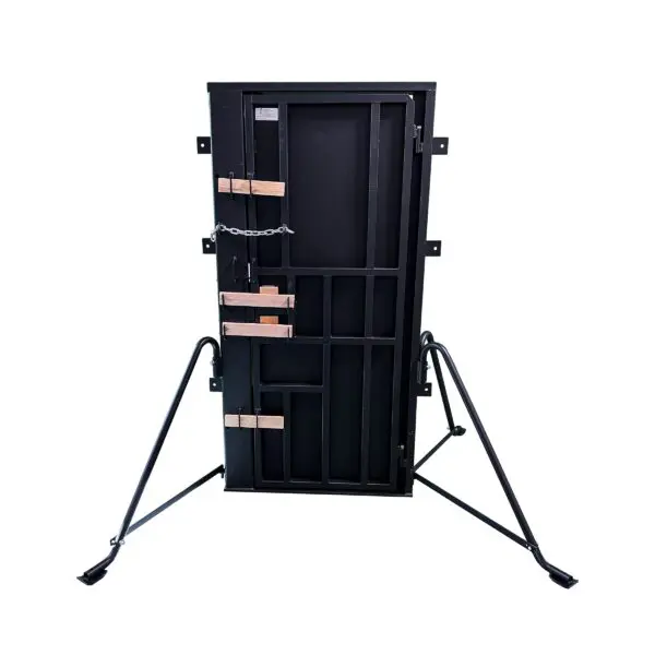 A black metal ALL-IN-ONE BREACHING TRAINING DOOR GEN1 with chains and wooden slats, standing on a folding metal support frame, isolated on a white background.