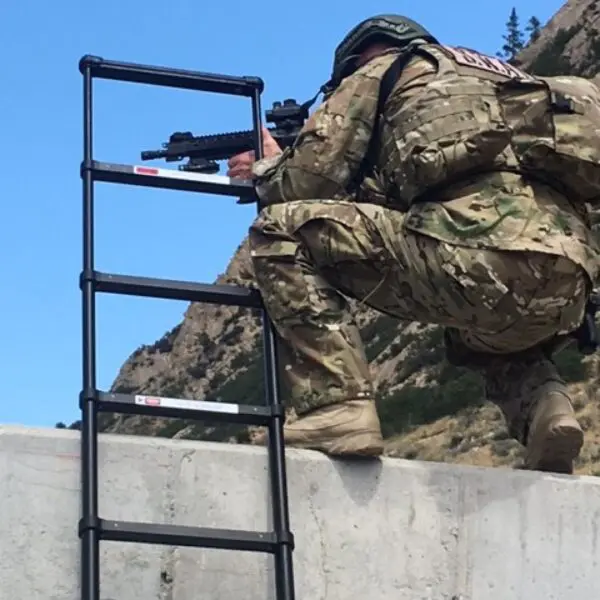 A man in camouflage is climbing up the side of a wall.